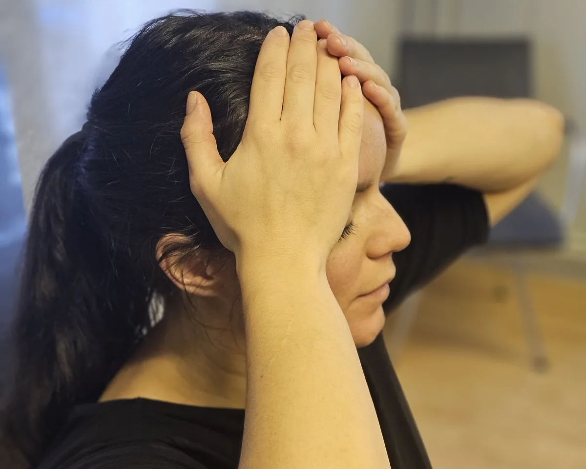 Kvinne som holder seg på hodet med lukkede øyne